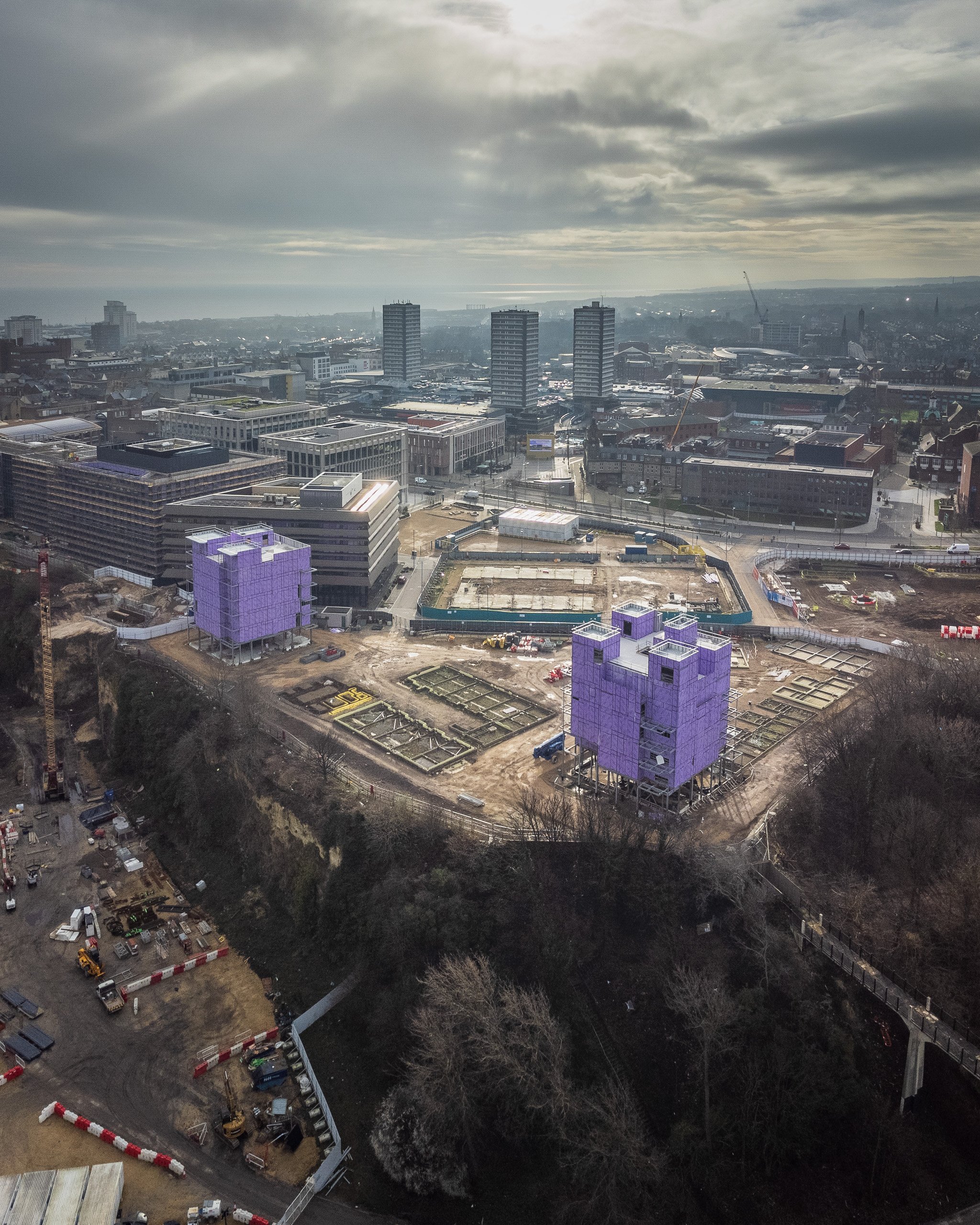 Aerial view of purple-wrapped modular buildings under construction on the Vaux Riverside development site, city tower blocks and coastline beyond.