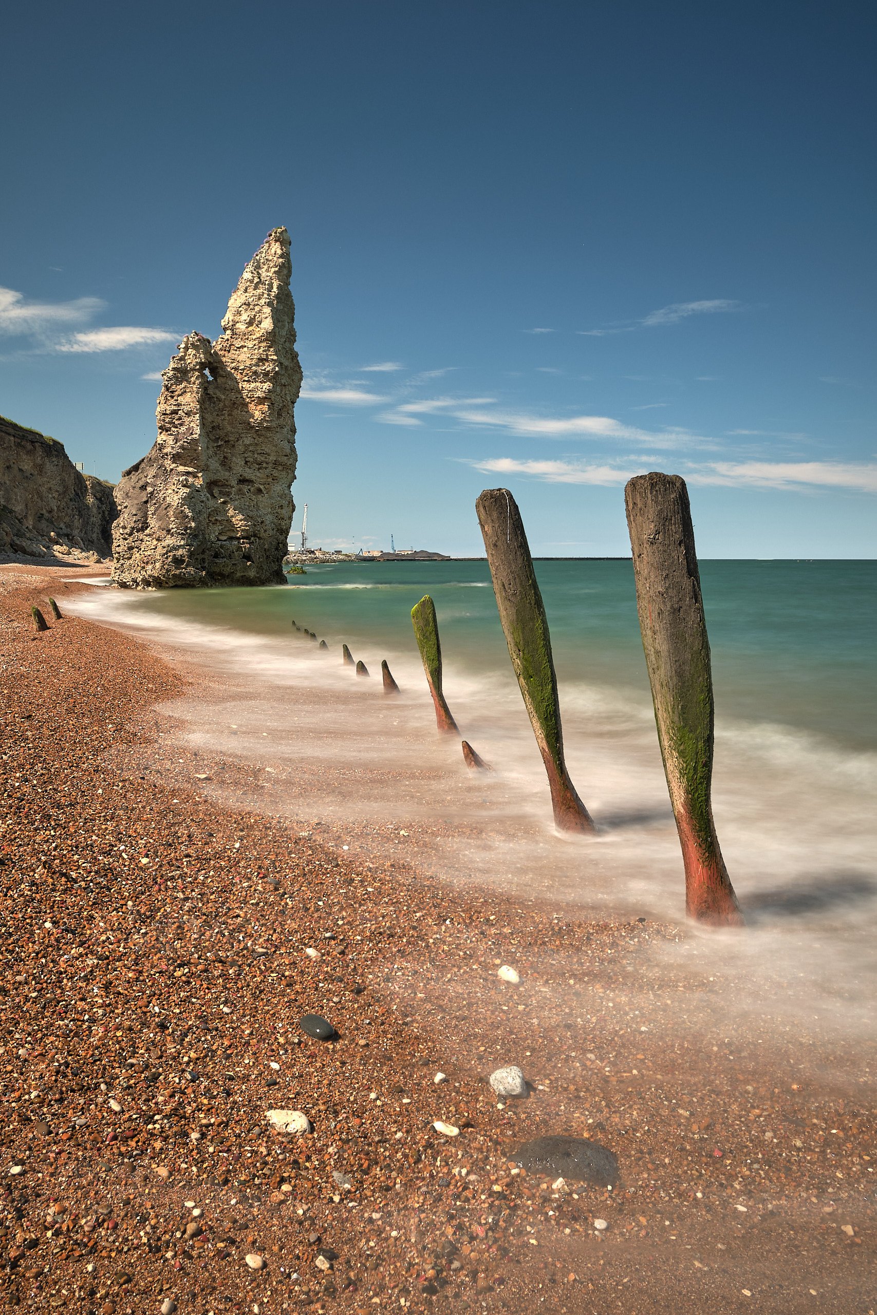Chalk sea stack and weathered wooden groynes on Seaham beach at low tide.