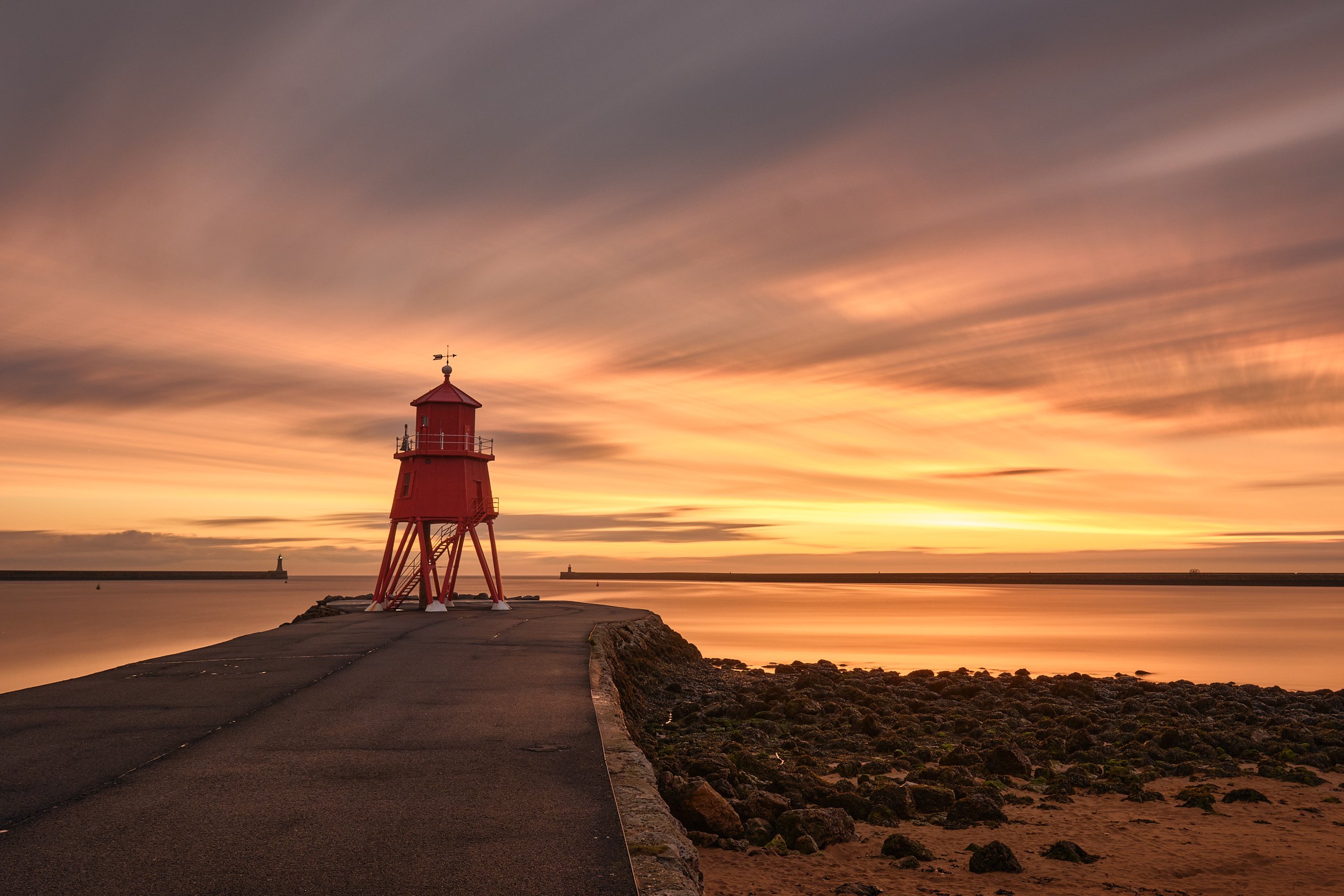 Herd Groyne lighthouse silhouetted against a warm sunrise sky over the rocks