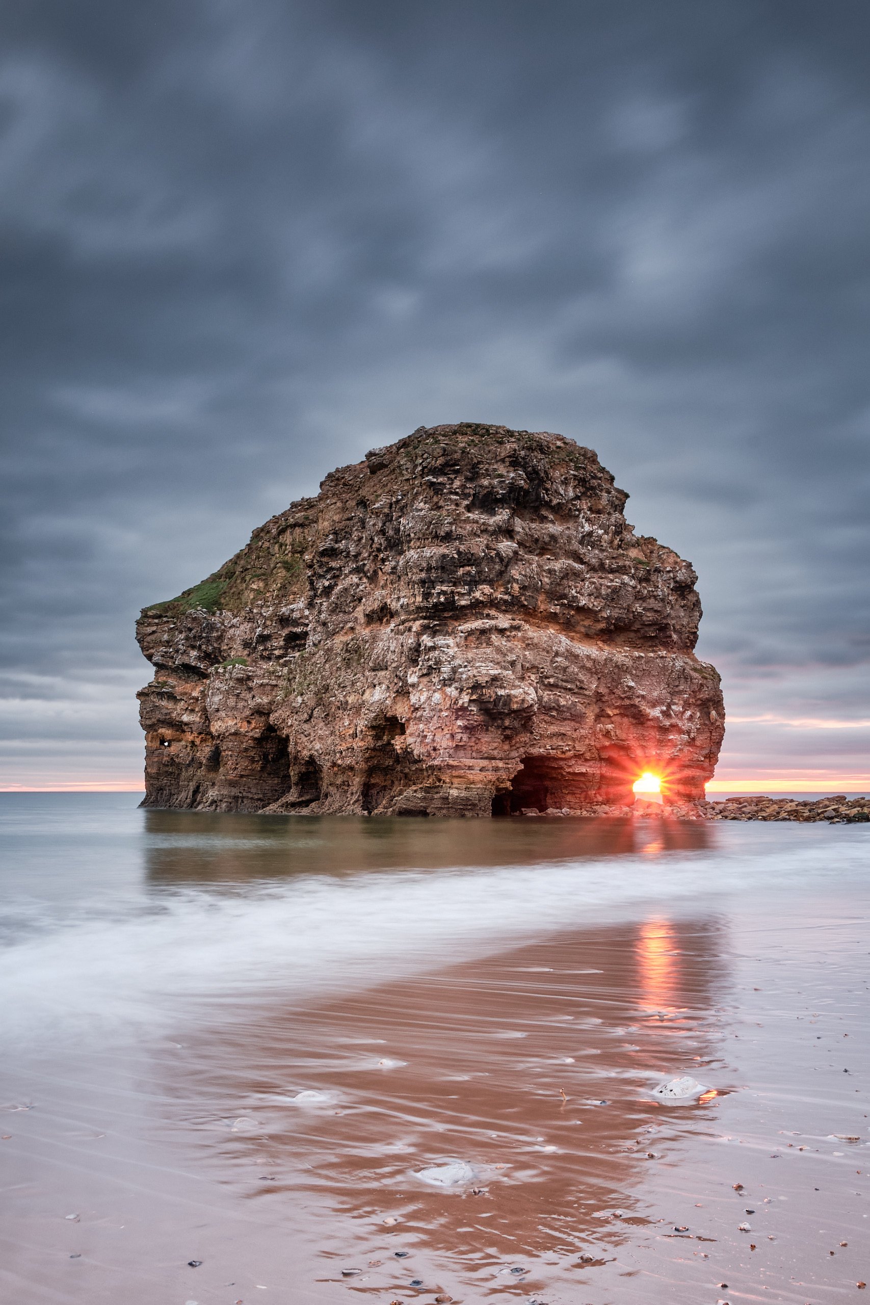 Sea stack at Marsden Bay with sunset light flaring through the rock arch