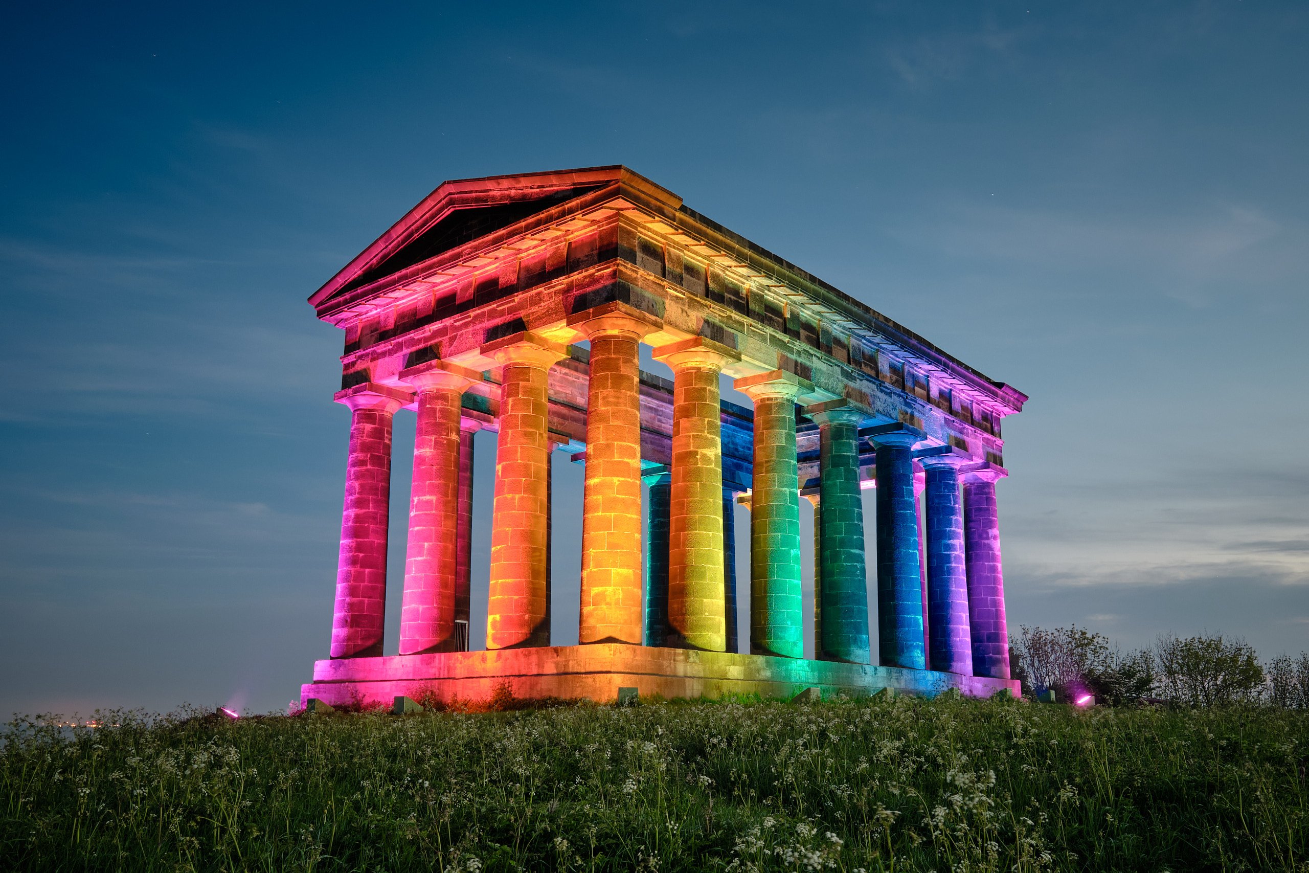 Penshaw Monument columns lit in rainbow Pride colours at dusk