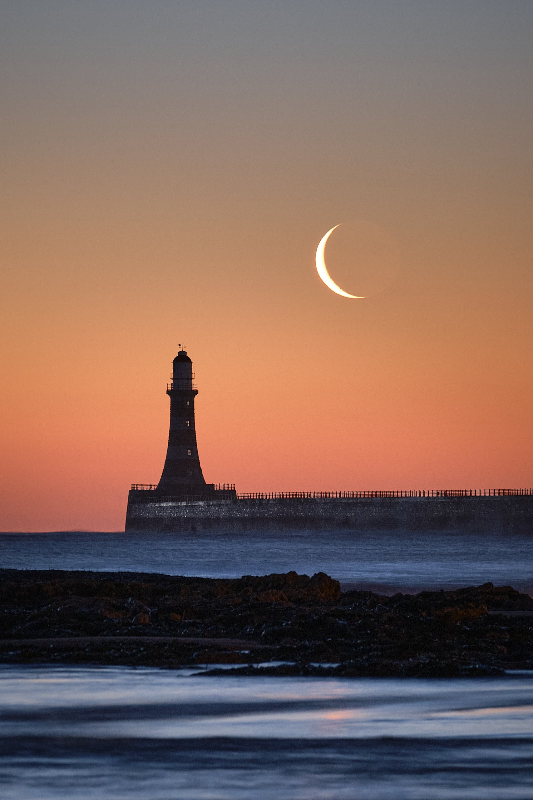Roker Pier lighthouse silhouetted beneath a crescent moon before sunrise