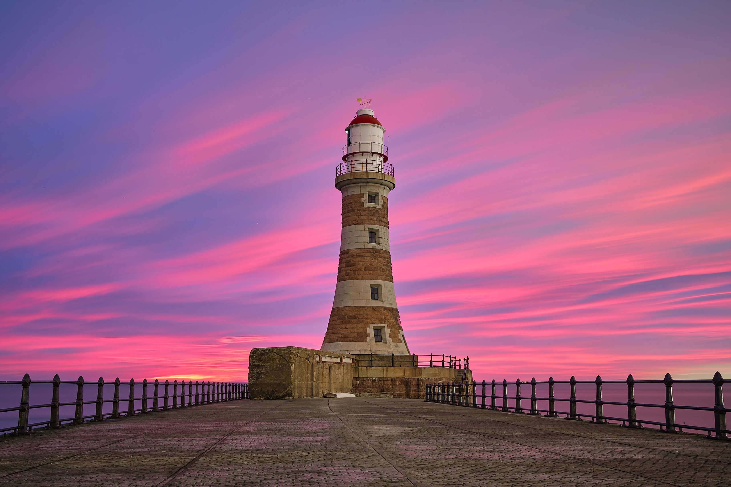Roker Pier lighthouse viewed straight down the pier walkway under a vivid pink and purple sunrise sky