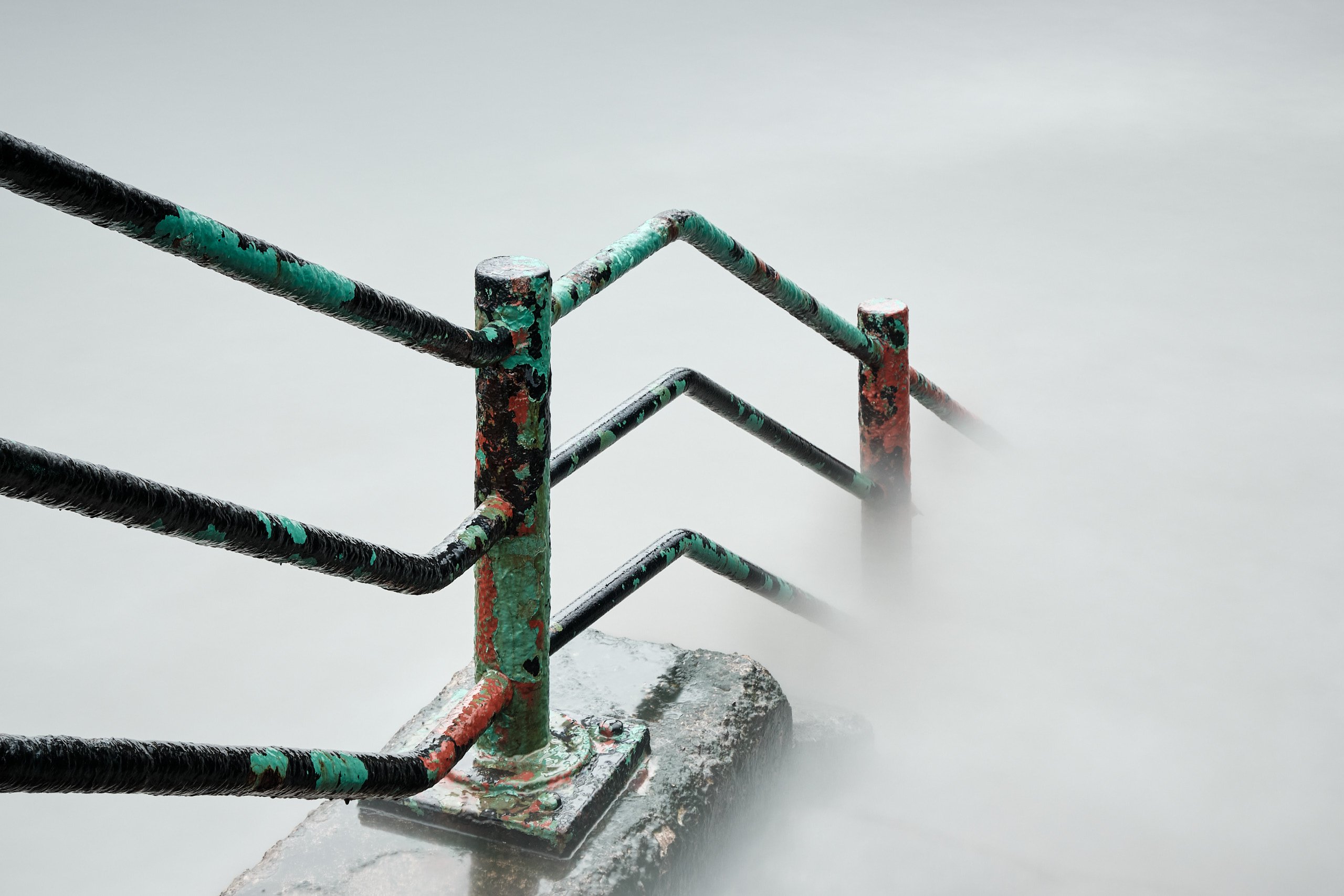 Weathered pier railings emerging from sea mist at high tide, Roker