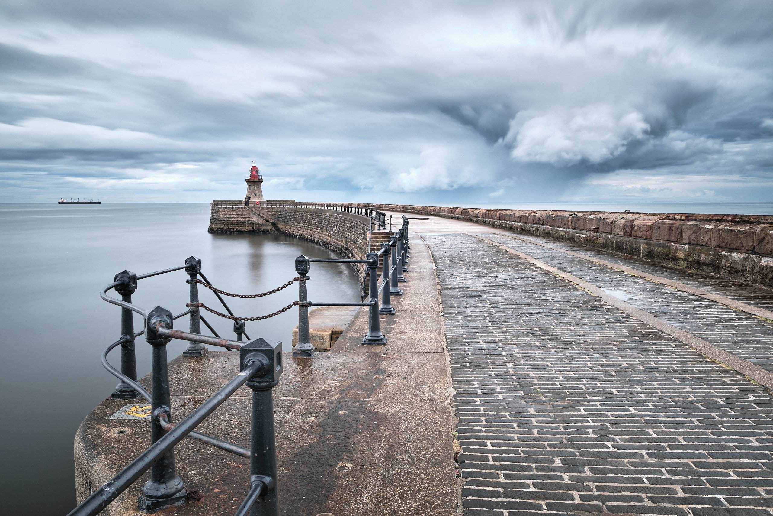 South Shields pier and lighthouse beneath dramatic storm clouds, with a cargo ship on the horizon