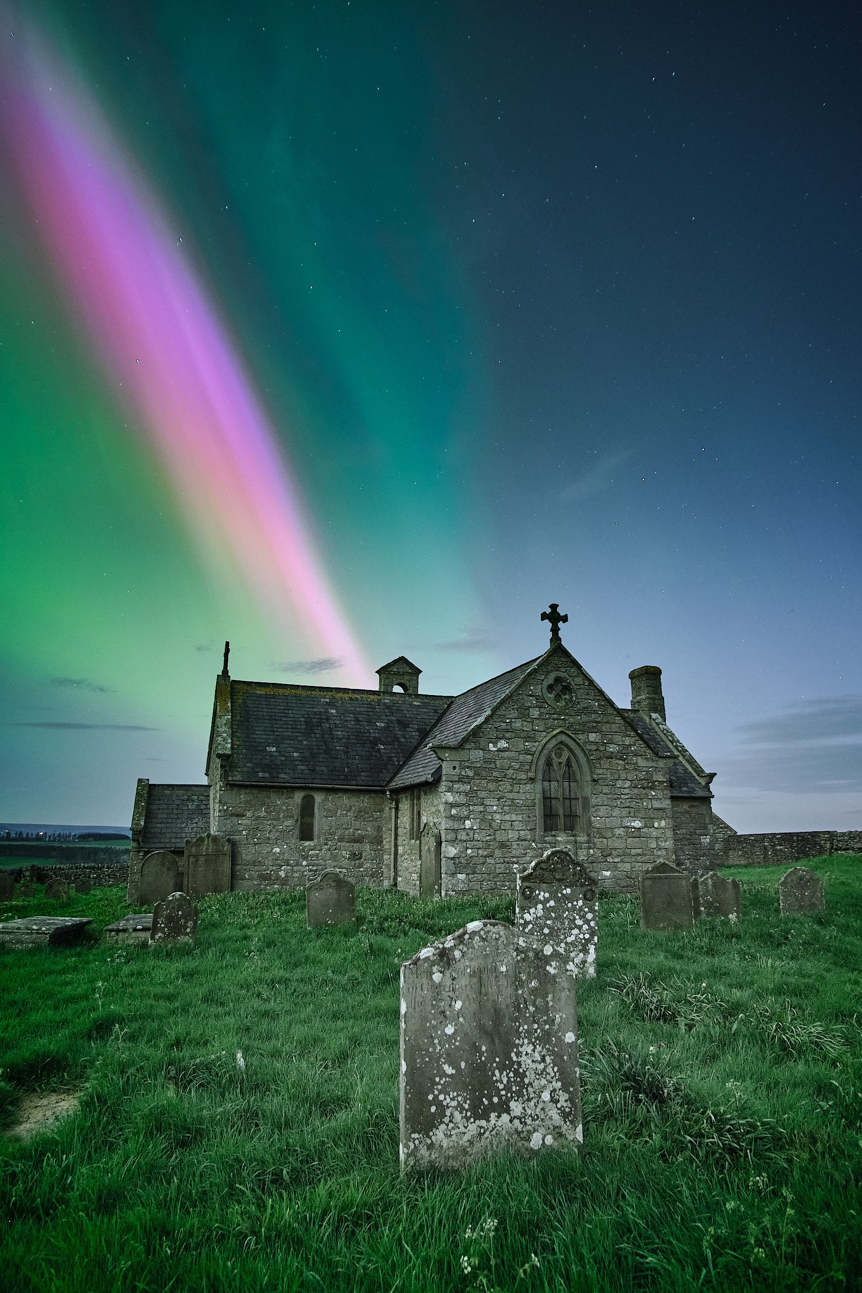 Aurora borealis in green and pink over St Andrew's Church and graveyard