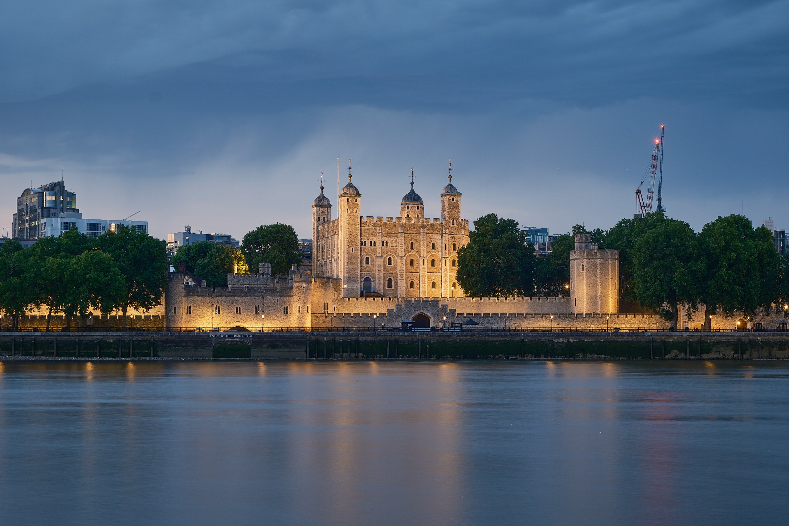 Tower of London walls and turrets lit against the Thames at dusk